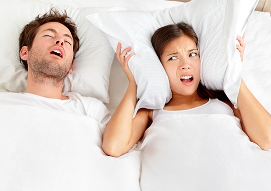 Woman covering ears in bed next to snoring man