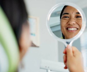 Woman smiling at reflection in handheld mirror