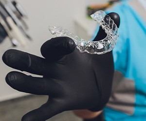 Dentist with black gloves holding clear aligner