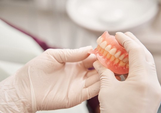 White-gloved hands holding complete set of dentures