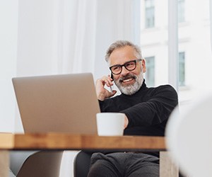 Man with glasses smiling while working on laptop