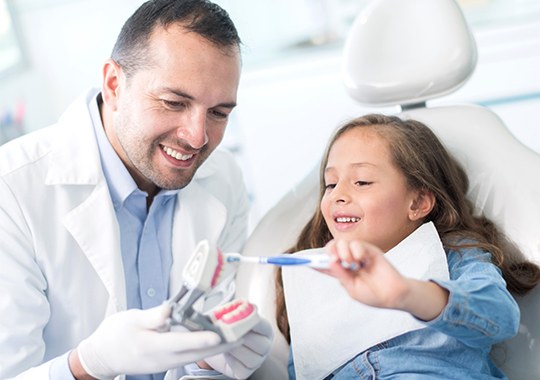 Dentist showing child how to brush her teeth