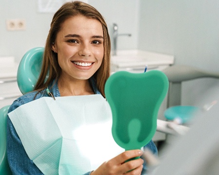 Woman smiling in mirror after dental implant salvage in Hammonton, NJ