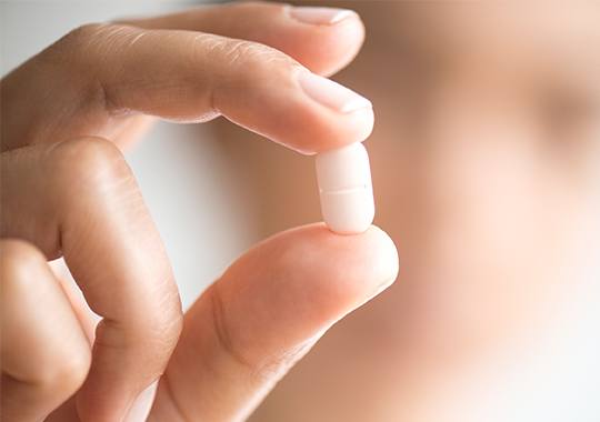 Hand holding a white tablet pill