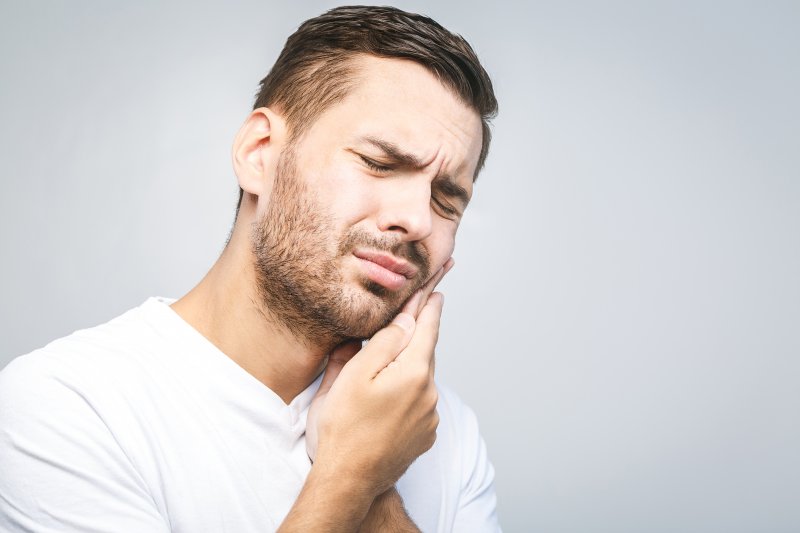 person holding their tooth and wincing in pain