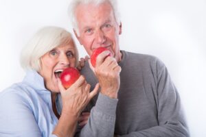 Older man and woman about to bite into apples.